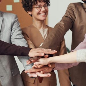 A group of happy, diverse colleagues celebrating teamwork and cooperation with a group high five indoors.